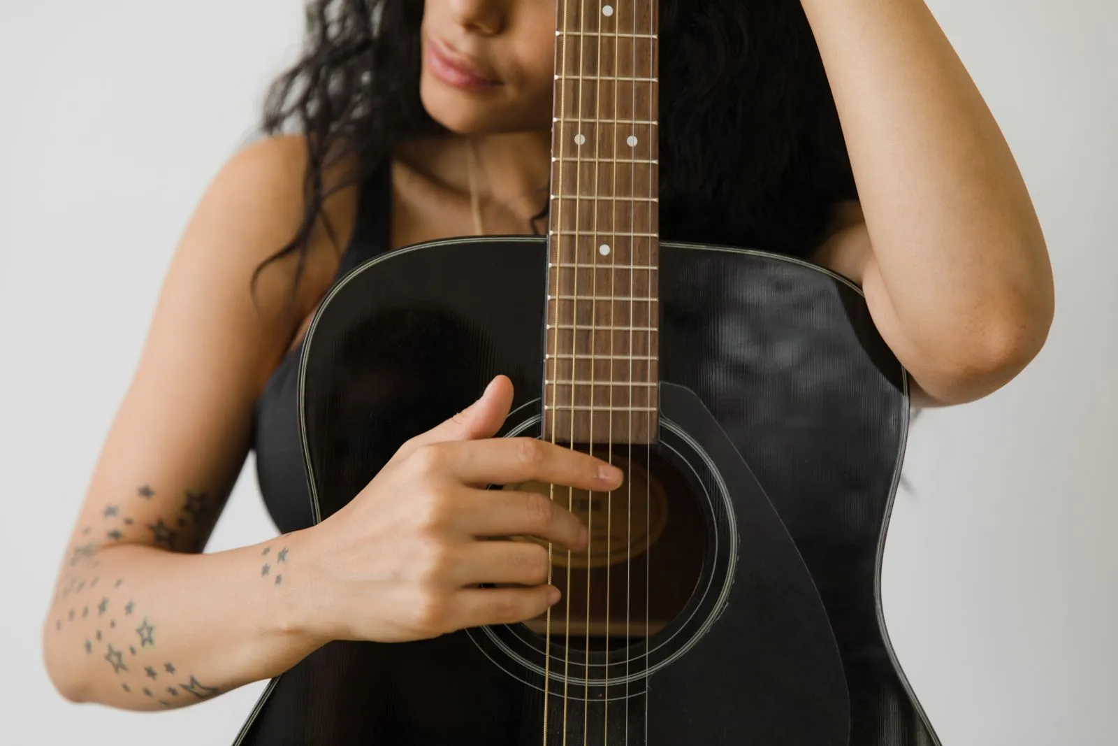 Tattooed woman strumming an acoustic guitar, focusing on hands and strings.